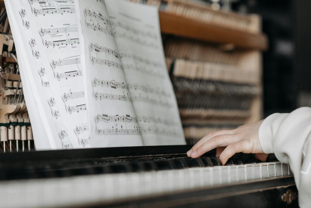 Close-up of child playing piano with sheet music. Focus on keys and notes.