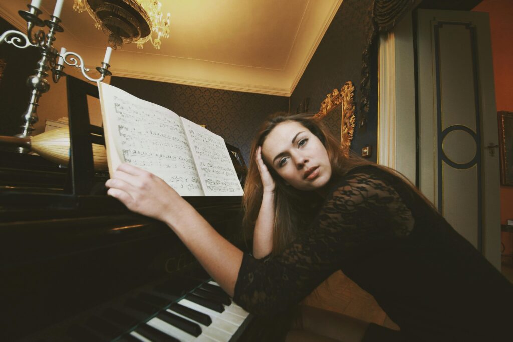 A woman in an elegant room poses next to a piano with sheet music. Warm lighting creates an intimate ambiance.