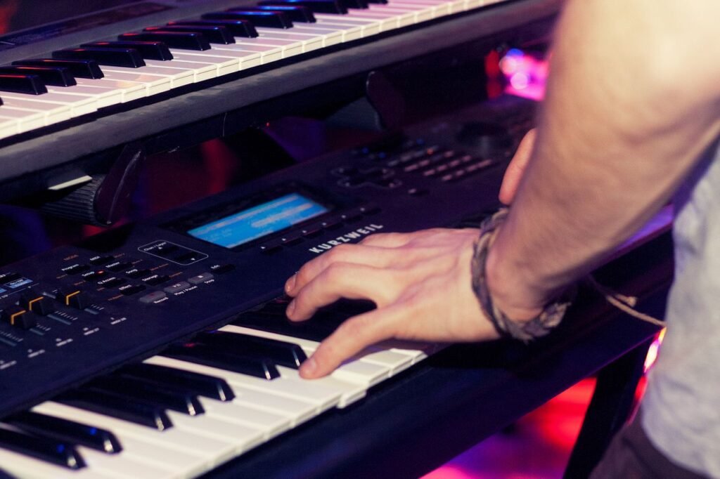 Musician's hands playing a keyboard in a dimly lit music studio, with vibrant lighting.