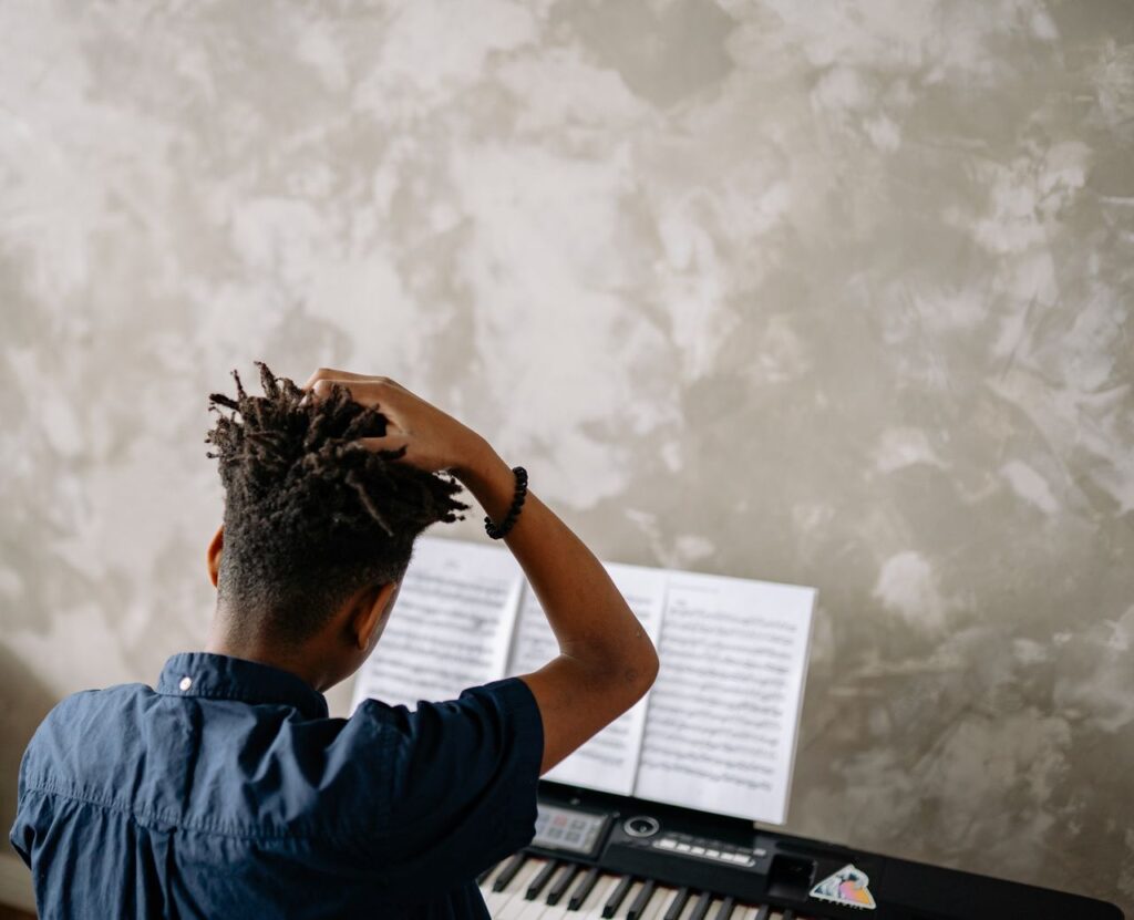 A child with afro hair practicing piano indoors, focusing on music sheets.
